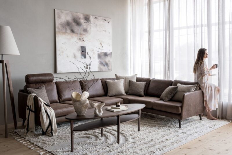 Brown Caramel leather sofa furnished with accessories and a girl drinking coffee next to it.